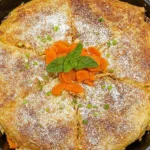 Moroccan chicken pastilla in a cast-iron skillet, golden crispy phyllo pie dusted with sugar and garnished with mint and apricots.