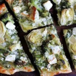 Green Pizza with Pesto, Feta, Artichokes, and Broccoli sliced into wedges with creamy feta, tender artichokes, and pesto on a golden crust.