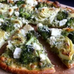 Green Pizza with Pesto, Feta, Artichokes, and Broccoli on a wooden board, topped with roasted broccoli, artichokes, and crumbled feta.