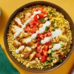 Lemon Dill Chicken & Couscous Bowls with spiced chicken, tomato salad, cucumbers, sliced almonds, and garlicky yogurt sauce drizzled on top.