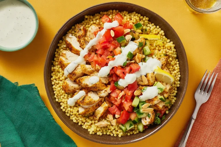Lemon Dill Chicken & Couscous Bowls with spiced chicken, tomato salad, cucumbers, sliced almonds, and garlicky yogurt sauce drizzled on top.