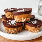 Peanut Butter Oat Cups stacked on a white plate with chocolate tops, creamy peanut butter filling, oat base, and flaky sea salt.