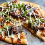 Short Rib Pizza with Smoked Gouda Cream Sauce topped with tender short ribs, arugula, red onion, and a creamy drizzle on a crispy crust.