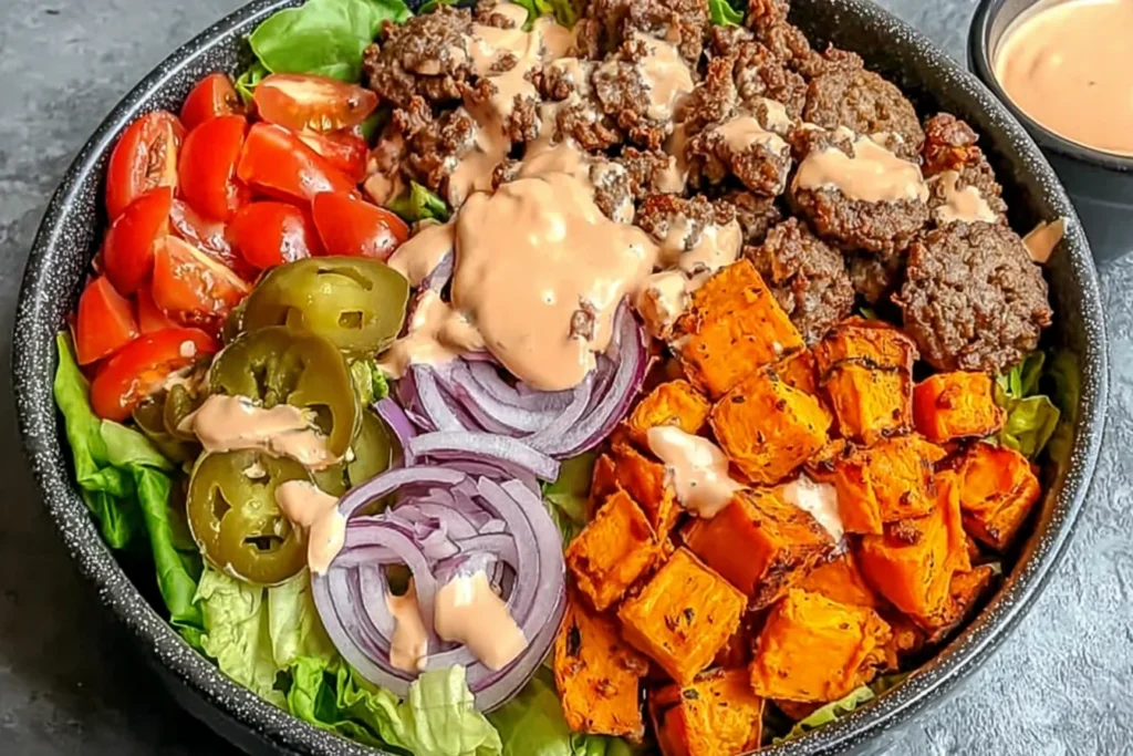 Sweet Potato Burger Bowl with seasoned ground beef, roasted sweet potato cubes, lettuce, tomatoes, pickles, red onion, and special sauce drizzle.