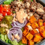 Sweet Potato Burger Bowl with seasoned ground beef, roasted sweet potato cubes, lettuce, tomatoes, pickles, red onion, and special sauce drizzle.