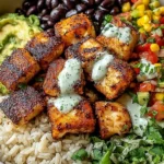 Fish Taco Buddha Bowl with blackened white fish, brown rice, black beans, corn salsa, guacamole, fresh herbs, and creamy ranch drizzle.