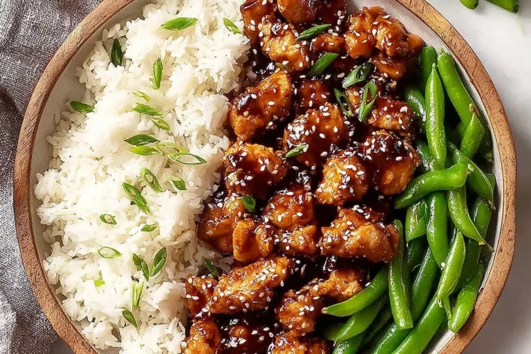 Asian High Protein Sesame Chicken bowl with glossy sesame glaze, white rice, and crisp green beans, topped with sesame seeds and scallions.