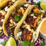Blackened Fish Tacos stuffed with spicy blackened fish, shredded purple cabbage, cilantro, crumbled cheese, and creamy chipotle sauce with lime wedges.