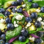 Blueberry Pistachio Spring Salad with baby spinach, fresh blueberries, cucumber slices, red onion, feta crumbles, and pistachios with balsamic dressing.