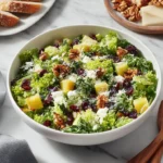 Ina Garten Cape Cod Salad Recipe in a white bowl with leafy greens, dried cranberries, toasted walnuts, apple chunks, and crumbled blue cheese.