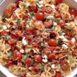 Cherry Tomato Bruschetta Pasta Salad with bowtie pasta, marinated cherry tomatoes, basil ribbons, crumbled cheese, and balsamic drizzle in a white bowl.