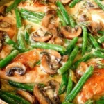 Chicken and Green Beans in Creamy Mushroom Sauce simmering in a skillet with browned chicken, fresh green beans, and sliced mushrooms in a creamy garlic-Parmesan sauce.