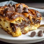 Chocolate Croissant Breakfast Bake slice with melty chocolate drizzle and chocolate chips on a plate, golden and custardy.