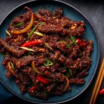 Crispy Chilli Beef Recipe plated with sticky sweet-spicy sauce, crispy beef strips, sliced red chilies, onions, and scallions.