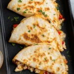 Healthy Baked Chicken Quesadilla folded and golden-brown on a baking tray with melty cheese, salsa, lime wedges, and sour cream.