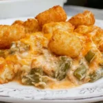 Green Bean Casserole with Tater Tots topped with crispy golden tots, melted cheese, and creamy green beans on a white plate.