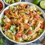 Taco Chicken Salad in a bowl with romaine, shredded chicken, black beans, tomatoes, cheddar, tortilla strips, and fresh lime.