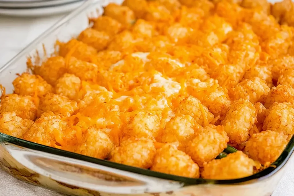 Baked Green Bean Casserole with Tater Tots in a glass dish, topped with crispy golden tater tots and melted cheddar cheese.