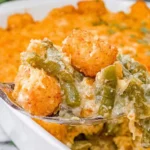 Spoonful of Green Bean Casserole with Tater Tots showing creamy green beans, melted cheese, and crispy golden tater tots in a baking dish.