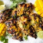 Grilled Mango Lime Chicken on a platter with charred edges, fresh cilantro, lime wedges, and sliced mango.