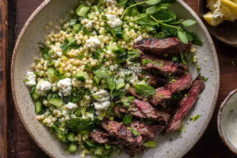 Grilled Skirt Steak with Lemon Herb Couscous Salad in a bowl with cucumber, fresh herbs, feta, and sliced grilled skirt steak.