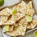 Key Lime Pie Yogurt Bark pieces on a tray with lime slices, topped with graham cracker crumbs and toasted coconut.