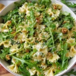 Lemon Arugula Pasta Salad in a white bowl with farfalle, peppery arugula, toasted walnuts, lemon dressing, and grated Parmesan.