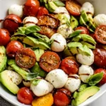 Light Avocado Caprese Salad with cherry tomatoes, mozzarella balls, sliced avocado, fresh basil, olive oil, and balsamic glaze in a white bowl.