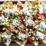 Loaded Vegetarian Greek Pita Nachos on a sheet pan with crispy pita triangles, cucumbers, tomatoes, olives, feta, and creamy tzatziki drizzle.