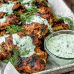 Mediterranean Grilled Chicken Thighs drizzled with dill yogurt sauce on a serving tray with fresh dill and a bowl of creamy herb sauce.