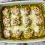 Pesto Baked Turkey Meatballs in a white baking dish, coated in basil pesto and topped with melted mozzarella cheese.