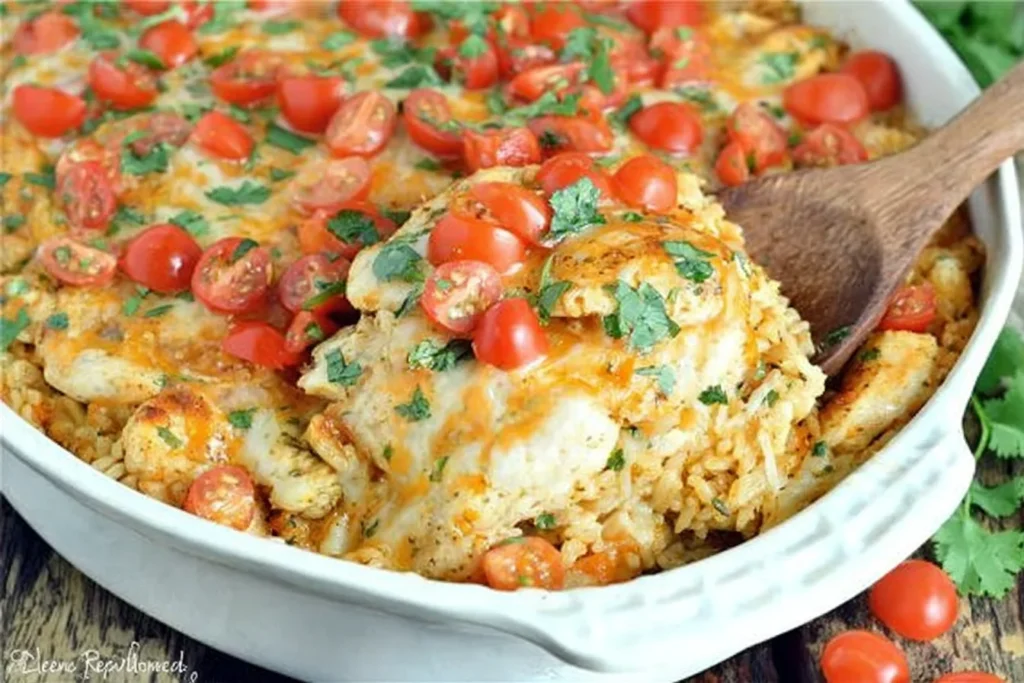 Queso Chicken and Rice Bake served from a white casserole dish with melty cheese, cherry tomatoes, and cilantro on top.