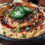Spicy Roasted Jalapeño Cowboy Cream Cheese Dip in a black bowl with BBQ swirl, sliced jalapeños, herbs, and tortilla chips.