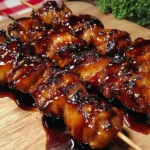 Grilled Chicken Yakitori Skewers glazed in a sticky soy-mirin sauce with charred edges, sprinkled with sesame seeds on a wooden board.