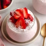 Cottage Cheese Strawberry Cheesecake Chia Seed Pudding in a glass topped with fresh sliced strawberries and a sprinkle of crushed ice on a plate.