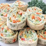 Veggie Pinwheels with Broccoli and Carrots stacked on a serving plate with creamy vegan filling, colorful veggie spirals, and kale garnish.