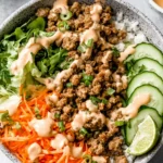 Banh Mi Bowl with saucy ground beef, sliced cucumbers, shredded carrots, fresh herbs, and creamy sriracha mayo over rice with a lime wedge.