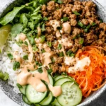 Banh Mi Bowl with sticky ginger-garlic beef, cucumber, shredded carrots, fresh herbs, and creamy sriracha mayo over rice.