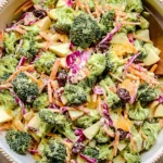 Broccoli Crunch Salad in a large serving bowl with fresh broccoli, apples, carrots, red cabbage, cranberries, and creamy yogurt dressing.