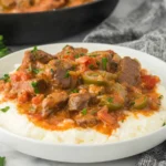 Cajun Grillades and Grits served in a white bowl with tender beef gravy, peppers, tomatoes, and parsley over creamy grits.