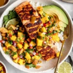 Cajun Salmon with Mango Salsa bowl with blackened salmon, white rice, avocado slices, lime, and fresh mango salsa with cilantro and red onion.