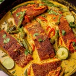 Caribbean-Style Coconut Curry Salmon seared in a skillet with creamy coconut curry sauce, peppers, herbs, and fresh lime wedges.