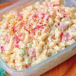Cheddar Sour Cream Macaroni Salad in a clear container, creamy pasta salad with diced red pepper, celery, and herbs, chilled and ready for potlucks.