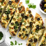 Olive Cheese Bread sliced on a baking sheet with melted Monterey Jack, green and black olives, and fresh parsley garnish.