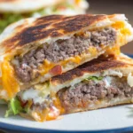 Quesadilla burger cut in half showing juicy ground beef and melted cheese inside a crispy tortilla, served with shredded lettuce.