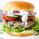 Chicken Burgers with Feta Cheese & Spinach stacked on a brioche bun with lettuce, tomato, cucumber, red onion, and tzatziki sauce.
