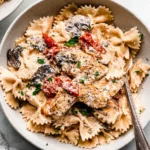 Bowl of Macaroni Grill’s Chicken Pasta Milano with creamy bowtie pasta, sliced chicken, mushrooms, sun-dried tomatoes, and Parmesan.
