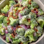 Sweet Classic Broccoli Salad in a bowl with creamy mayo dressing, crispy bacon, red onion, dried cranberries, and crunchy seeds.