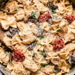 Creamy Macaroni Grill’s Chicken Pasta Milano with bowtie pasta, chicken, mushrooms, sun-dried tomatoes, and Parmesan in a skillet.