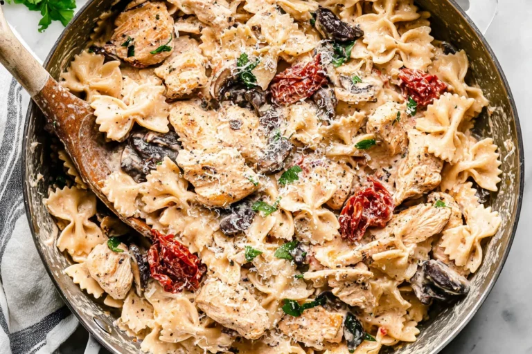 Creamy Macaroni Grill’s Chicken Pasta Milano with bowtie pasta, chicken, mushrooms, sun-dried tomatoes, and Parmesan in a skillet.
